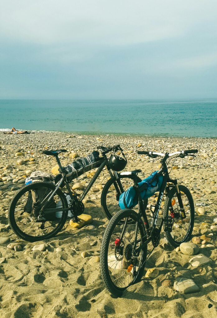Two bicycles parked on a rocky beach by the calm sea on a sunny day, ideal for leisure travel.