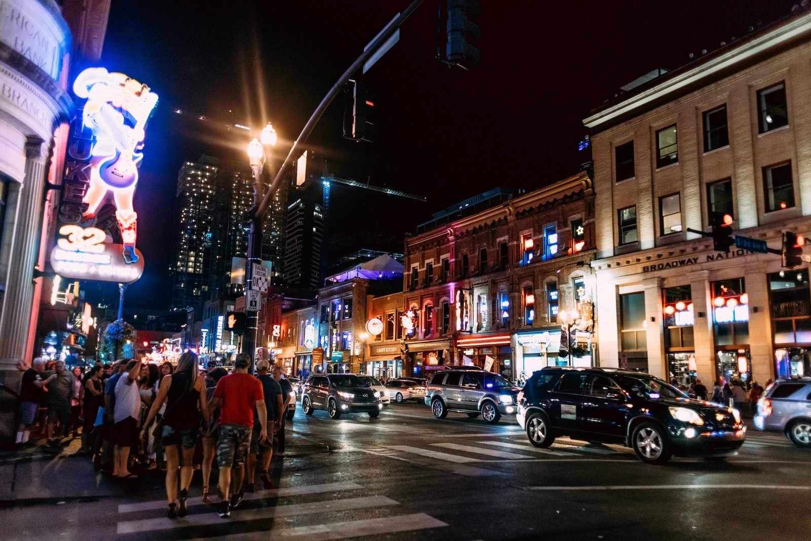 A lively downtown street scene with neon lights, people, and traffic, captured at night.